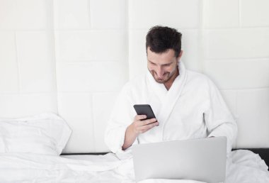 Telefonunu yatak kullanan genç adam.