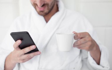 Telefonunu yatak kullanan genç adam.