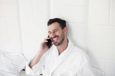 Telefonunu yatak kullanan genç adam.