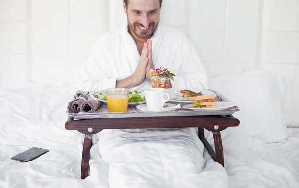 Happy single man eating breakfast in bed