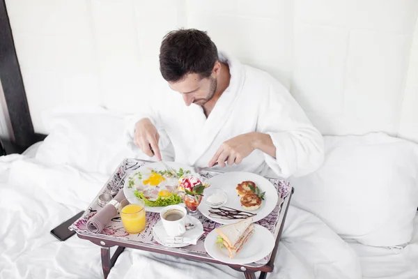 Happy single man eating breakfast in bed