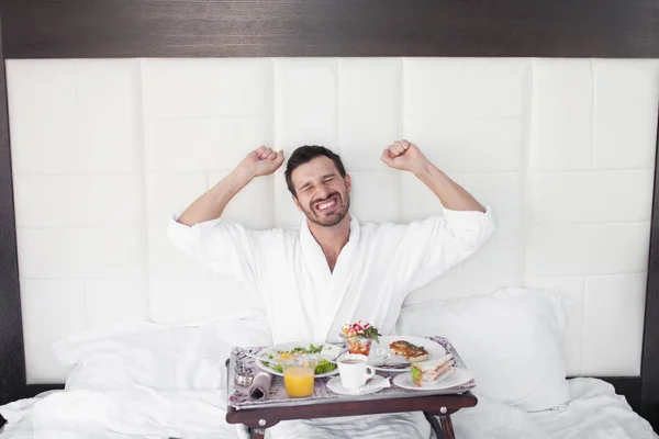 Happy single man eating breakfast in bed