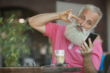 Bir neşeli ve şık olgun iş adamı smartphone üzerinde bir arkadaşıyla konuşurken bir gülümseme ile kel bir kafa ile duygusal portresi. Komuta sizde sakallı