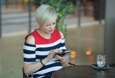 Orta yaşlı kadın oturur kafe manifatura ya da akıllı cep telefonu işletim