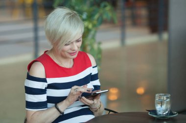 Orta yaşlı kadın oturur kafe manifatura ya da akıllı cep telefonu işletim