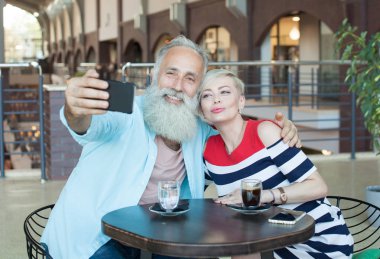 Üst düzey çift kafede bir telefonu kullanarak bir selfie yapar. Yılını kutluyor.