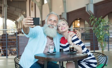 Üst düzey çift kafede bir telefonu kullanarak bir selfie yapar. Yılını kutluyor.