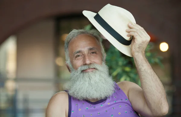 Closeup of hipster old man with beard and mustache wearing purple shirt and straw fedora hat.