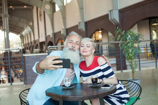 Senior couple makes a selfie using a phone in the cafe. Celebrating anniversary.