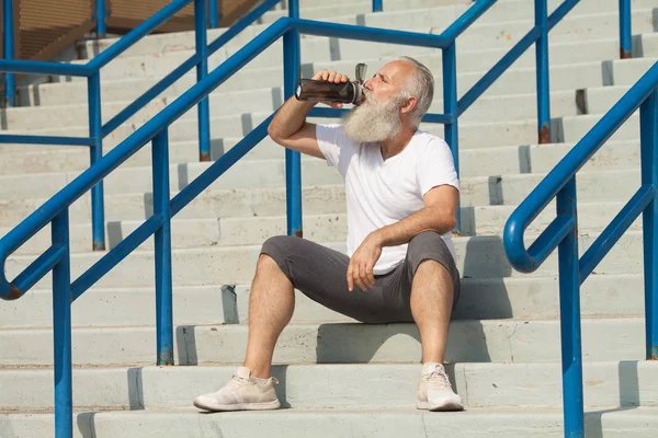 closeup grey bearded old man in white vest ready to do morning exercises drink water bottle