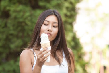Yeşil ağaçlar arka planda Park üzerinde dondurma yeme mutlu genç gülümseyen Asyalı esmer kadın.