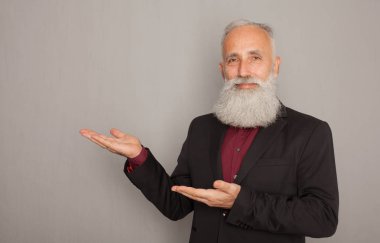 Sakallı ihtiyar bir şey üzerinde gri bir duvar sunarken cebine elini tutarak.