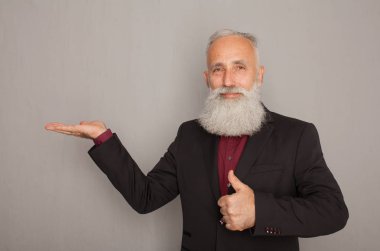 Sakallı ihtiyar bir şey üzerinde gri bir duvar sunarken cebine elini tutarak.