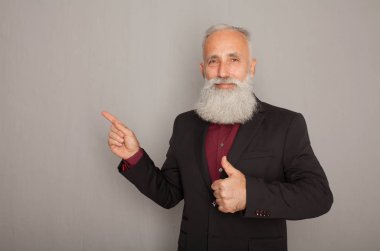 Parmak uzakta üzerinde gri arka plan işaret mutlu yaşlı sakallı işadamı portresi