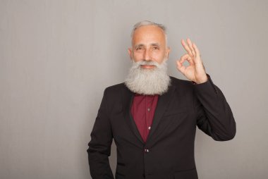 Tamam jest gösterilen ve üzerinde gri izole kamera için gülümseyen siyah elbiseli mutlu olgun adam.