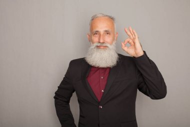 Tamam jest gösterilen ve üzerinde gri izole kamera için gülümseyen siyah elbiseli mutlu olgun adam.