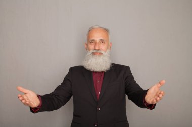 Sakallı ihtiyar bir şey üzerinde gri bir duvar sunarken cebine elini tutarak.