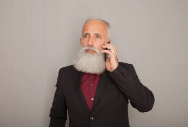Stüdyo gri arka plan ile cep telefonu kullanırken gülümseyen mutlu üst düzey sakallı iş adamı vurdu