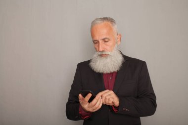 Mavi arka plan karşı onun cep telefonuna kısa mesaj okuma olgun adam portresi. Orta yaşlı beyaz erkek ayakta kopya alanı ile gri duvara.