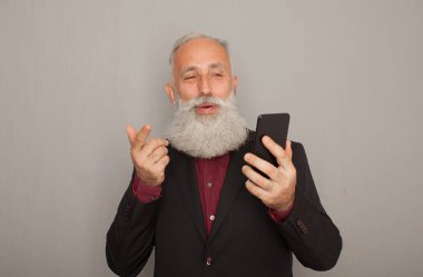 Stüdyo gri arka plan ile cep telefonu kullanırken gülümseyen mutlu üst düzey sakallı iş adamı vurdu