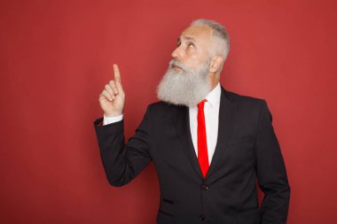 Elini boş alana kopyalayın. Takım elbise ve kravat işaretleme kopya alanı ve kırmızı bir arka plan karşı dururken gülümseyen kıdemli adam sakallı