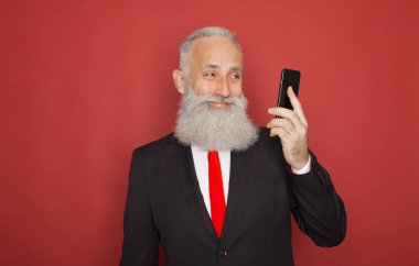 Kırmızı bir arka plan karşı cep telefonu kullanırken gülümseyen kıdemli mutlu sakallı işadamı stüdyo çekim