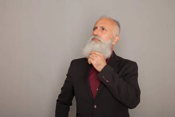 Bearded senior man thinking on grey background.