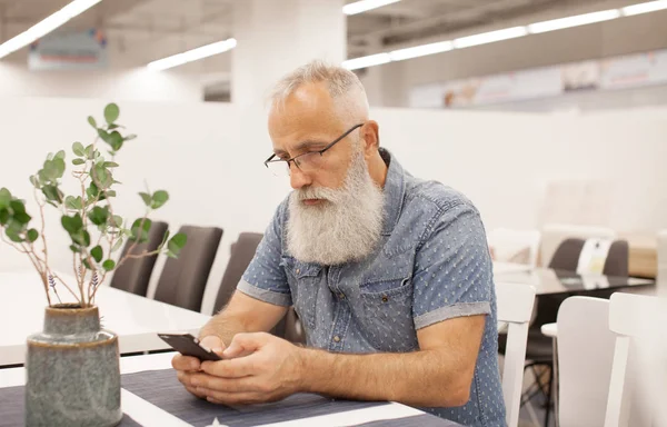 Handsome old man dressed in smart casual style and eyeglasses is using a smartphone while sitting at office.