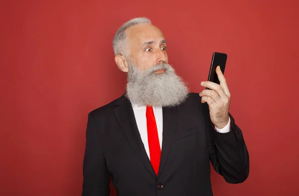 Porträtt Förvånad Skäggig Gubbe Kostym Med Mobiltelefon Isolerade Över Röd — Stockfoto