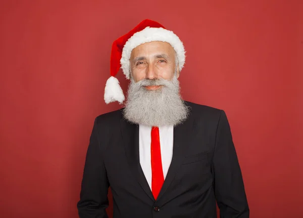 portrait of senior man in santa hat looking at camera and winking over red background