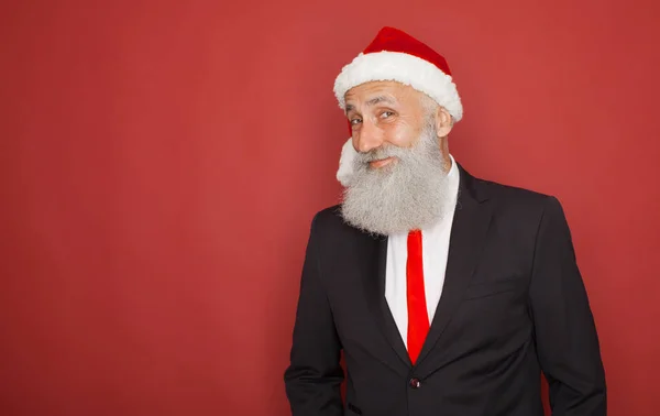 portrait of senior man in santa hat looking at camera and winking over red background