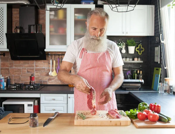 Bebaarde Senior Man Steaks Zijn Keuken Koken — Stockfoto