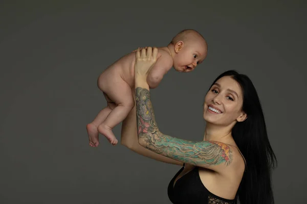 Madre Sostiene Bebé Sus Brazos Sobre Fondo Gris — Foto de Stock