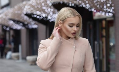 Şehir sokaklarında yürürken bir palto giyiyor güzel şık sarışın genç kadın. Trendy rahat kıyafet. Sokak moda