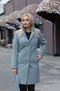 Şehir sokaklarında yürürken bir palto giyiyor güzel şık sarışın genç kadın. Trendy rahat kıyafet. Sokak moda