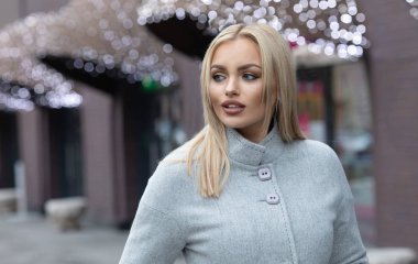 Şehir sokaklarında yürürken bir palto giyiyor güzel şık sarışın genç kadın. Trendy rahat kıyafet. Sokak moda