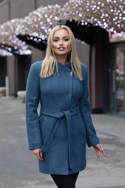 Şehir sokaklarında yürürken bir palto giyiyor güzel şık sarışın genç kadın. Trendy rahat kıyafet. Sokak moda