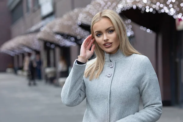 Şehir sokaklarında yürürken bir palto giyiyor güzel şık sarışın genç kadın. Trendy rahat kıyafet. Sokak moda