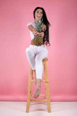 beautiful sexy young girl standing on a pink background with pineapple. clipart
