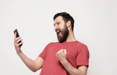 Cep telefonu kullanarak, gri arka plan üzerinde izole ayakta rahat giysiler giyen neşeli bir genç adamın Portresi.