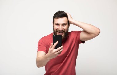 Cep telefonu kullanarak, gri arka plan üzerinde izole ayakta rahat giysiler giyen neşeli bir genç adamın Portresi.