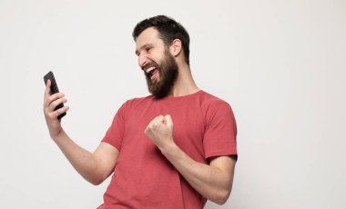 Cep telefonu kullanarak, gri arka plan üzerinde izole ayakta rahat giysiler giyen neşeli bir genç adamın Portresi.