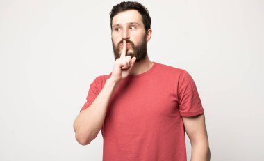 Endişeli ciddi adam dudaklarında işaret parmağı tutan rahat t-shirt giyen, sessiz kalmak ve noize yapmak değil isteyen. İnsan yüz ifadeleri