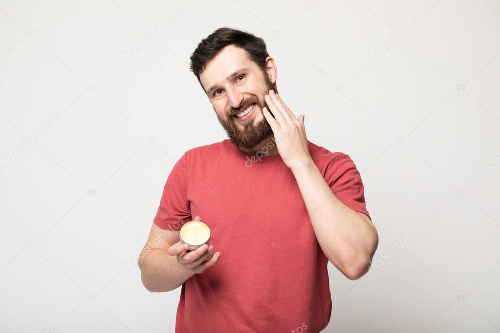 Close-up image of handsome bearded man holding beard balm.