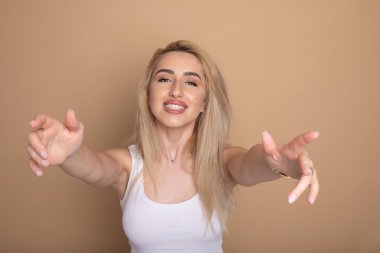 Dost görünümlü sarışın kadın kameraya doğru ellerini çeker, sıcak sarılmak verir, sevinçle gülümsüyor, en iyi arkadaşı ile sarılmak için gidiyor, beyaz rahat kıyafet giyer, bej arka plan üzerinde izole.