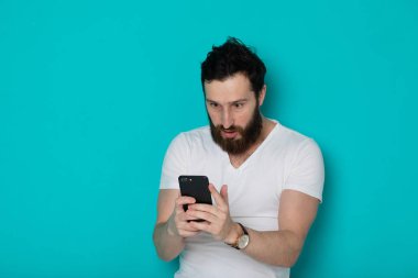 Mavi arka plan üzerinde izole cep telefonu bakarak sürpriz bir rahat adam Portresi