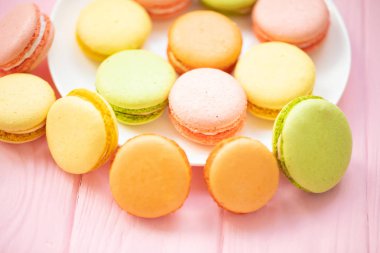 Renkli Fransız veya İtalyan makarnalar beyaz plaka üzerinde yığın arka plan için kopya alanı ile pembe ahşap masa üzerine koymak. Ikindi çayı veya kahve molası ile servis edilen tatlı.