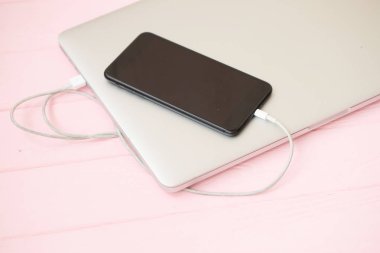 Cep telefonu pembe arka planda dizüstü bilgisayara bağlı.