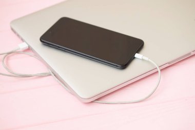 Cep telefonu pembe arka planda dizüstü bilgisayara bağlı.