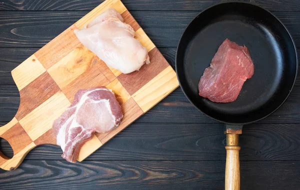 raw different meat on black cooking pan, top view. Wooden background.